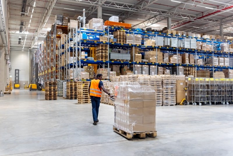 male dispatcher pulling pallet jack with boxes in warehouse